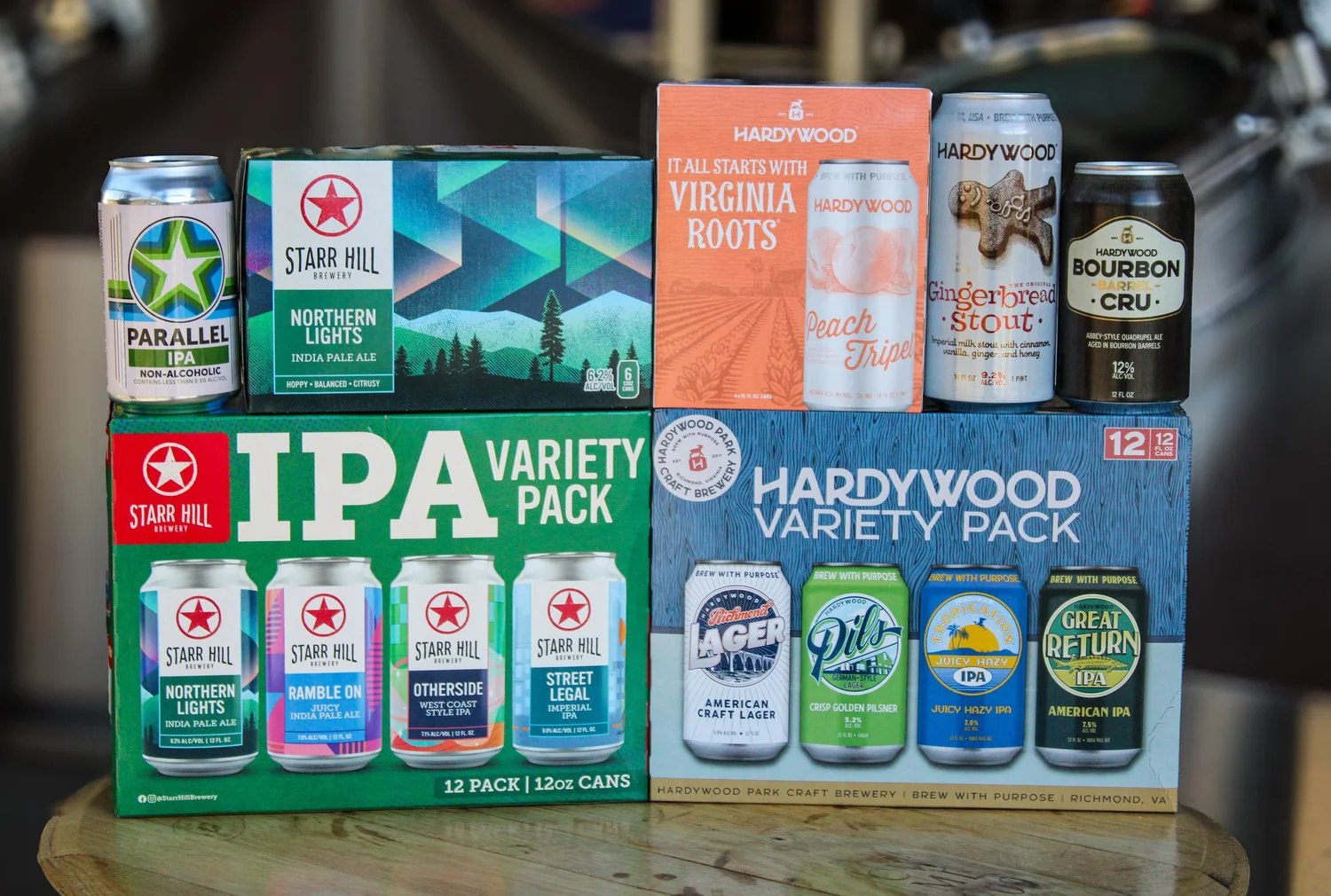 Packaged beer from both breweries staged together: a Starr Hill IPA Variety Pack and a Hardywood Variety Pack side by side, with cans of Parallel non-alcoholic IPA, Northern Lights IPA, Hardywood Peach Tripel, Gingerbread Stout and Bourbon Barrel Cru arranged above them.