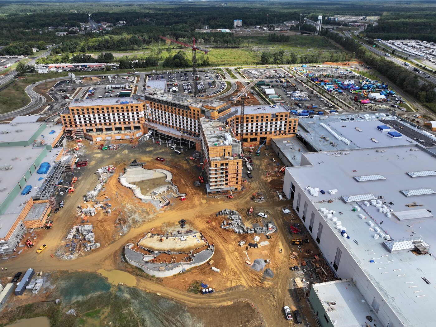 Wide aerial of the whole Kalahari Spotsylvania construction site: the hotel wings framed out in orange sheathing, the waterpark and convention buildings roofed to their west, and graded earth and equipment across the rest of the 135 acres.