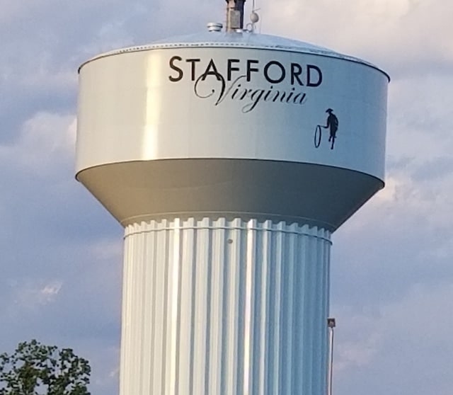 A Stafford County water tower against a blue sky with scattered cloud, lettered STAFFORD above the word Virginia in script, with a silhouette of a colonial figure rolling a hoop.